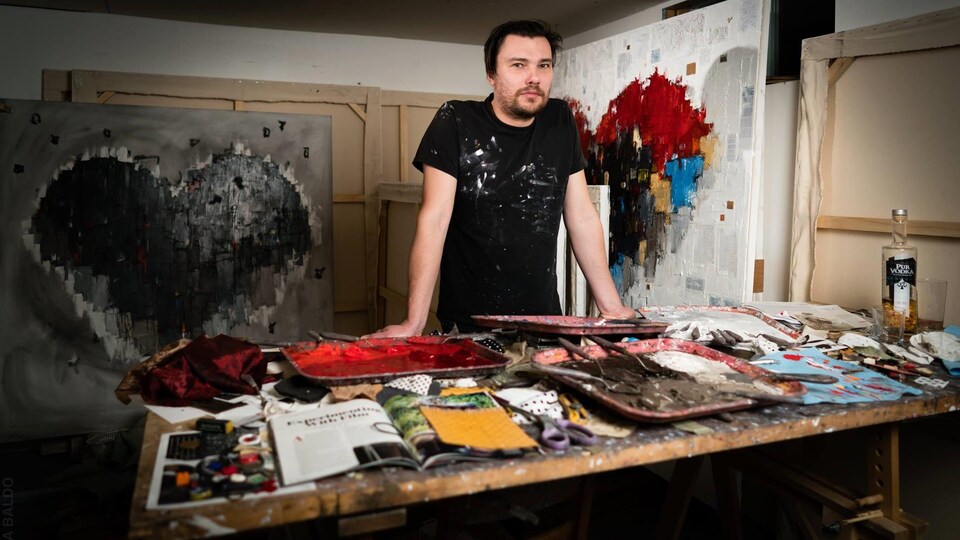 Un artiste dans son atelier devant des toiles représentant des coeurs colorés.