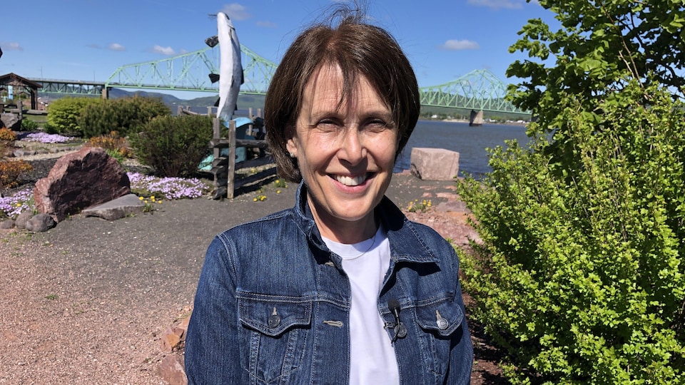 Smiling woman with brown hair in front of a river and a bridge.
