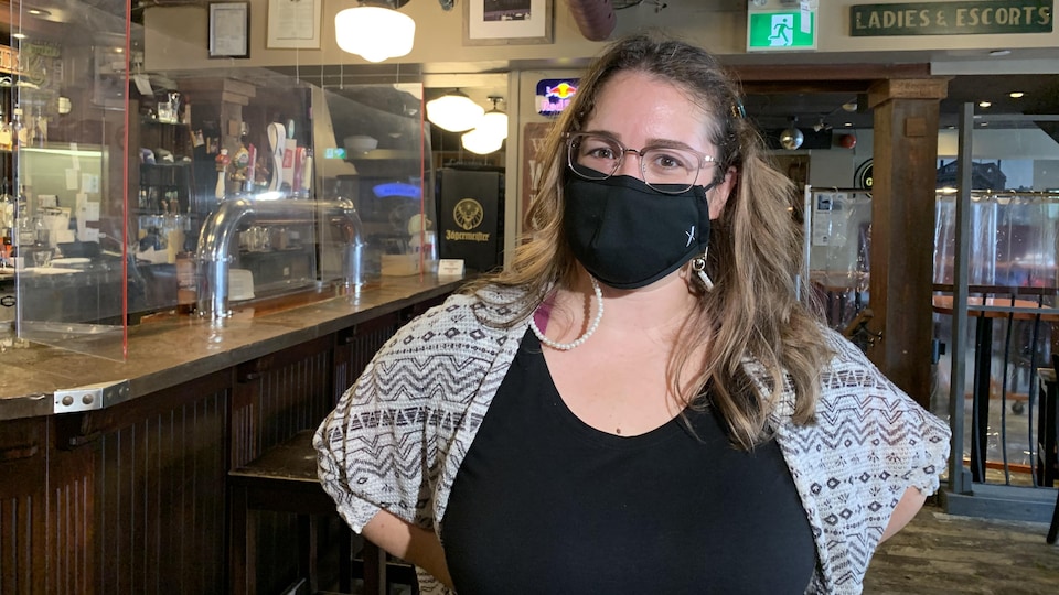 La femme, qui porte un couvre-visage noir, est debout devant un bar.