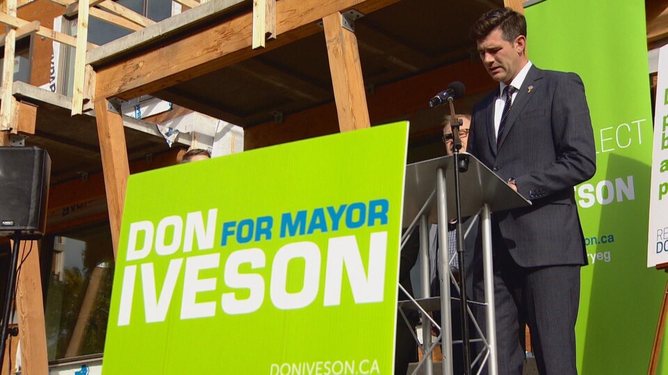 Don Iveson devant un lutrin et son affiche qui dit « Don Iveson comme maire »