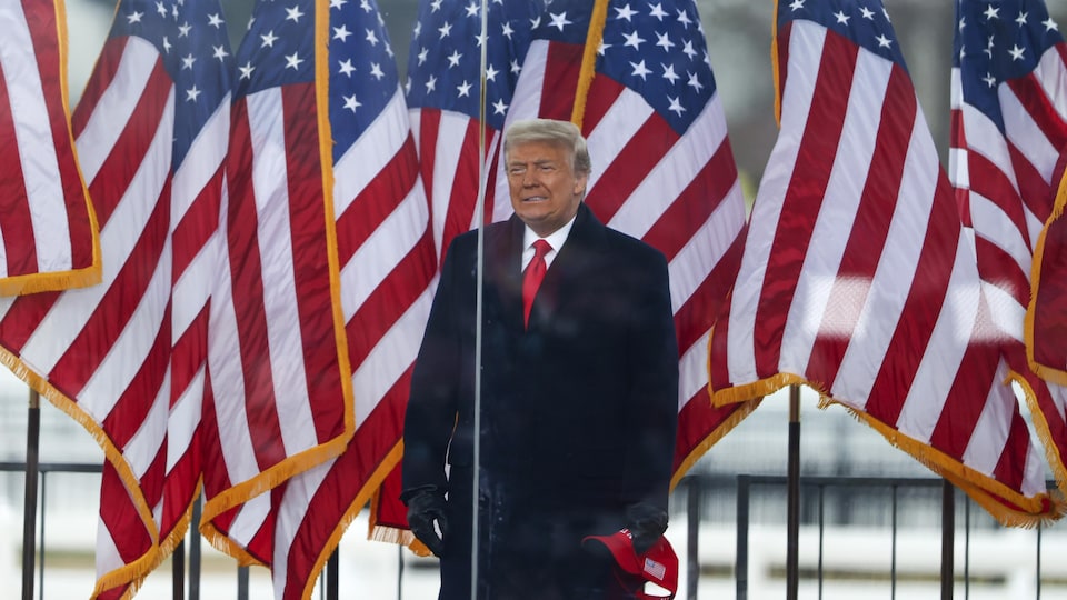 Il est debout devant des drapeaux américains.