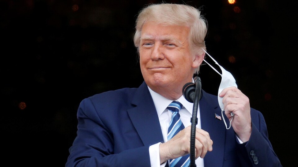 Donald Trump enlève le couvre-visage qu'il porte.