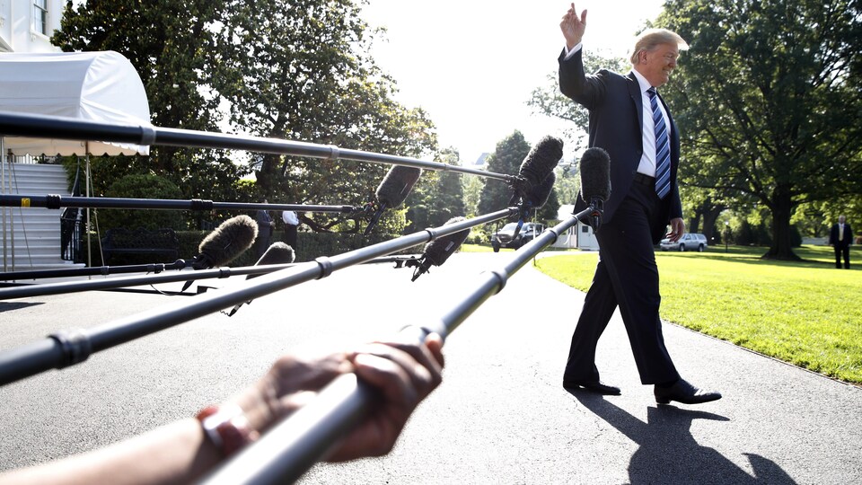 Donald Trump fait un geste de la main, devant des micros qui avaient été tendus devant lui.