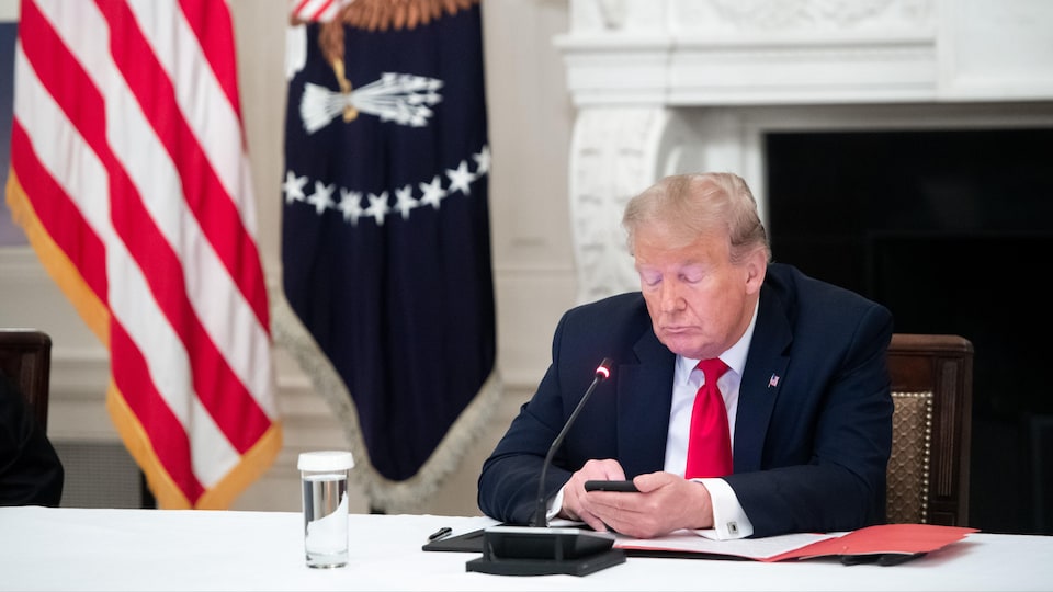 Donald Trump, assis à une table, regarde son téléphone portable.