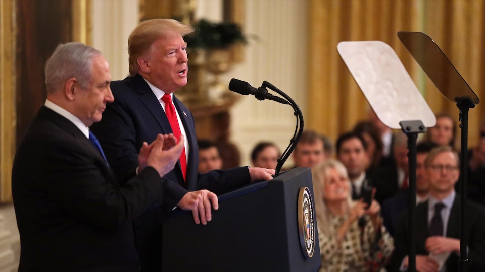Les deux hommes sont sur un podium duquel Donald Trump s'adresse à la presse.