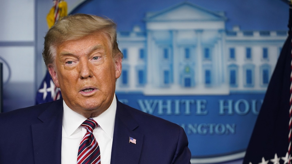 Donald Trump se tient devant une affiche de la Maison-Blanche.