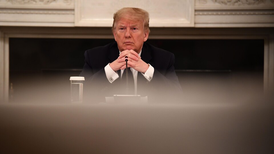 Donald Trump est assis à une table les mains croisées.