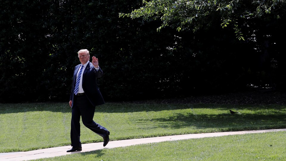 M. Trump marche sur un petit trottoir au milieu de la pelouse et envoie la main à la caméra.