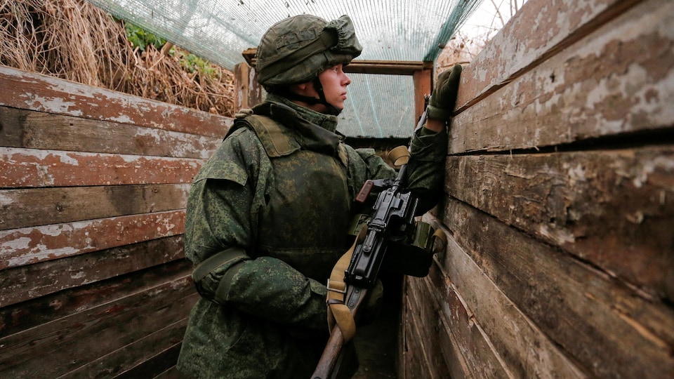 Un jeune soldat armé d'un fusil observe au loin depuis une tranchée.