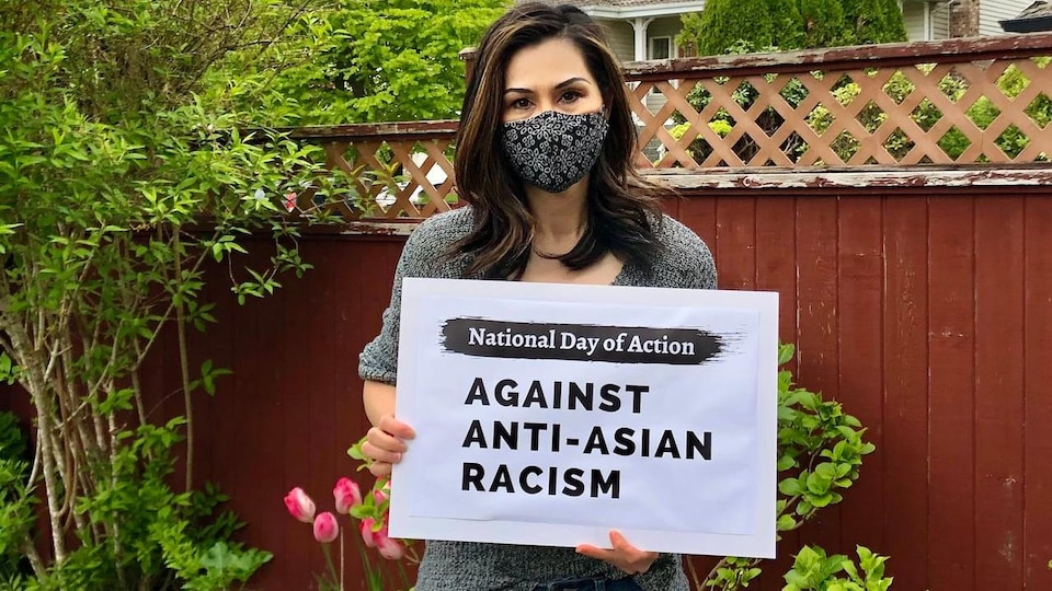 Doris Mah tient une affiche sur laquelle on lit : Journée d'action national contre le racisme anti-asiatique. 