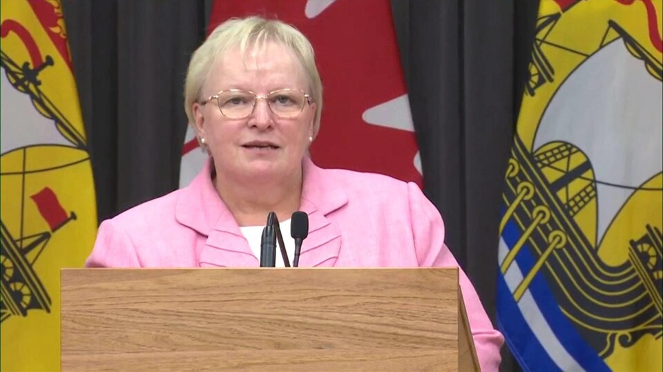 Dorothy Shephard répond à une question, debout devant des drapeaux du Nouveau-Brunswick.