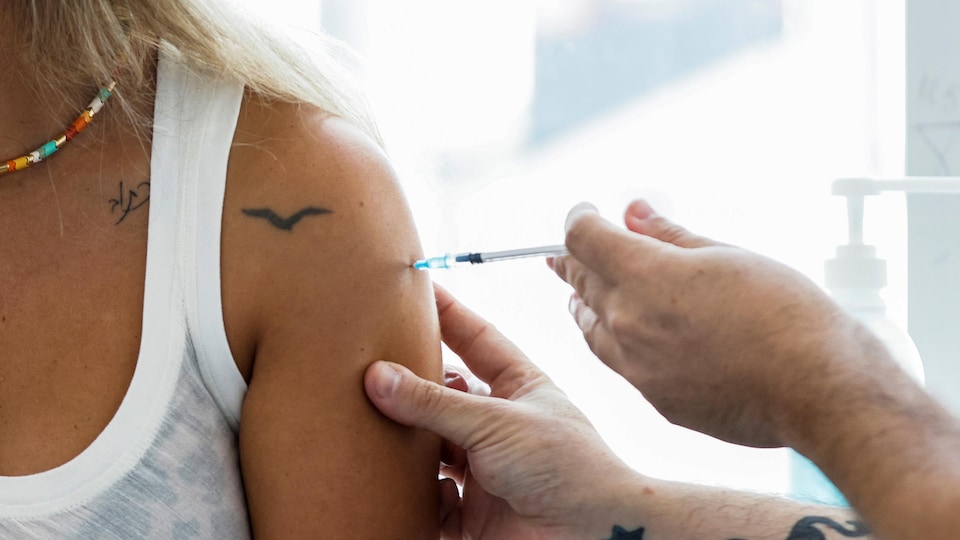 Plan rapproché du bras d'une femme en camisole pendant qu'elle se fait vacciner.