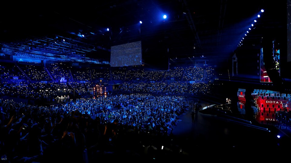 Une salle de spectacles est remplie de personnes. Les lumières sont tamisées bleues et tous les membres de la foule tiennent une petite lumière dans leur main.