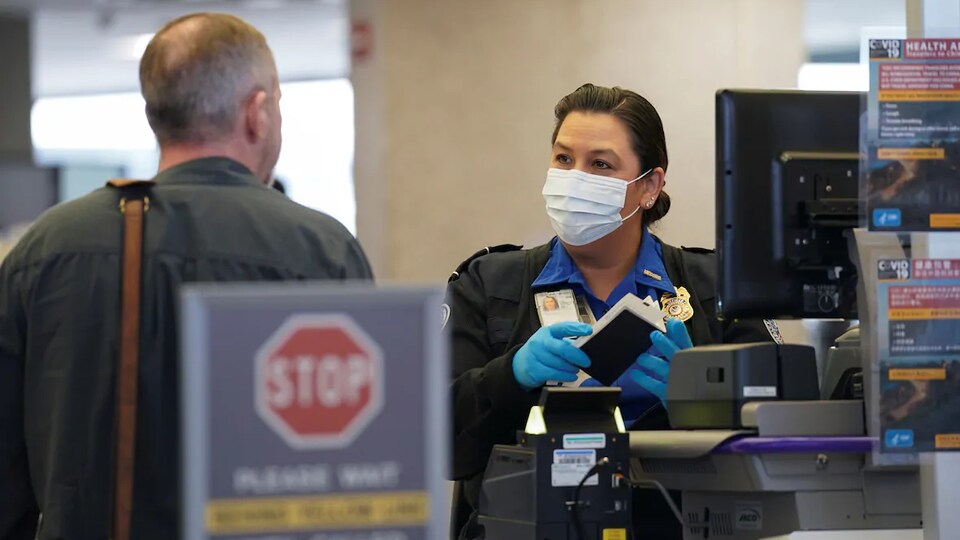 Une douanière américaine qui porte un masque regarde un voyageur.