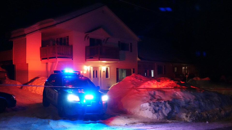 Une voiture de police stationnée dans l'entrée d'une maison à deux étages, la nuit.