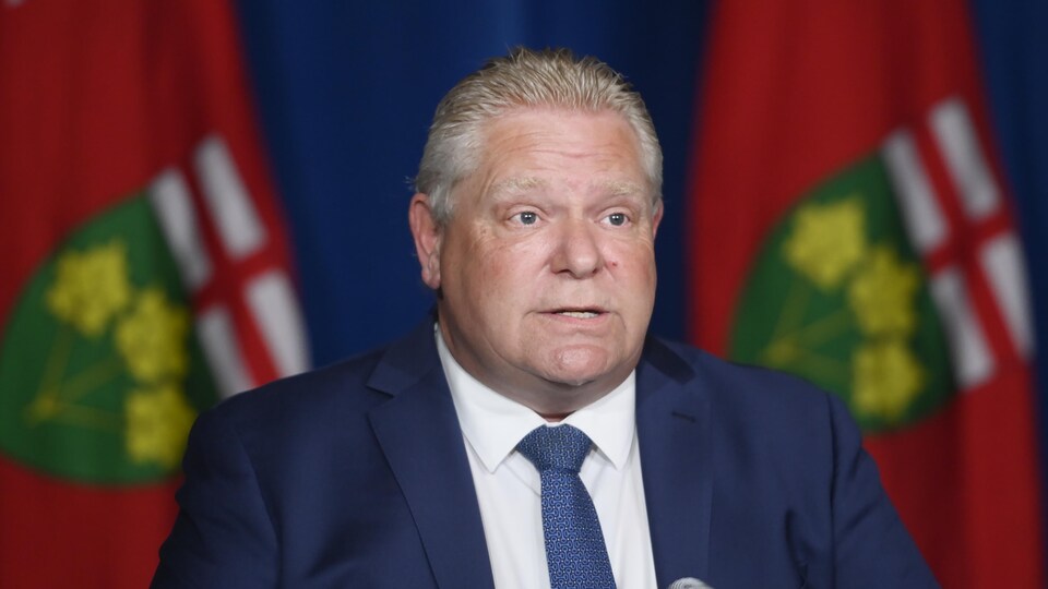 Doug Ford parle devant un présentoir avec un drapeau de l'Ontario derrière lui pour annoncer que les écoles de l'Ontario vont rester fermées.