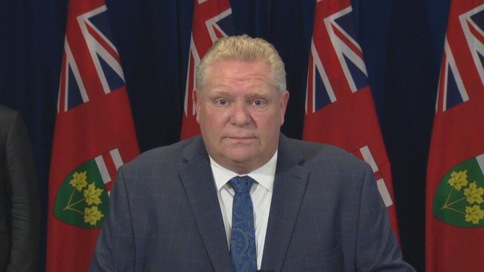 Doug Ford devant quatre drapeaux de l'Ontario.