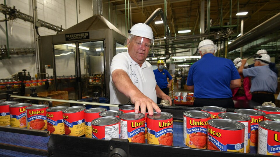 Le premier ministre Doug Ford regroupe des conserves de tomates sur un convoyeur dans une usine.