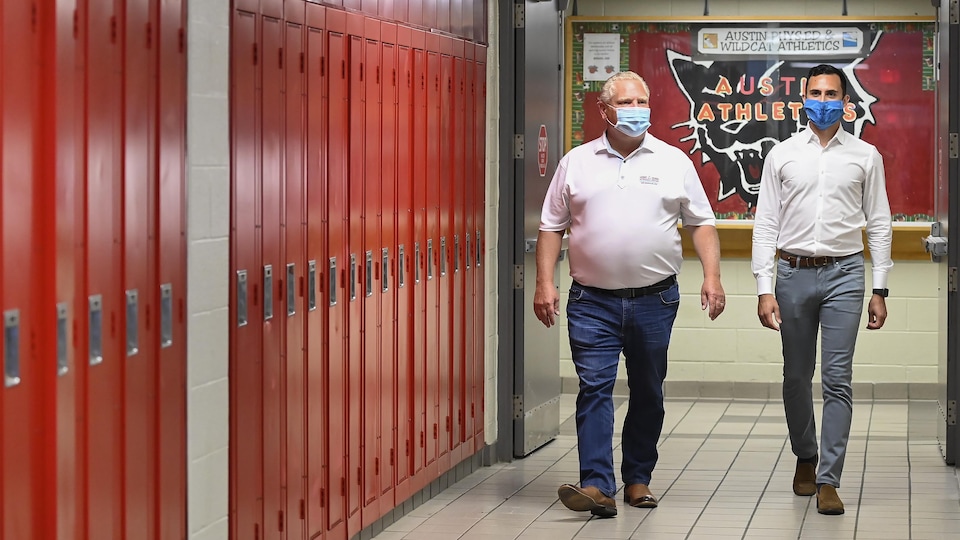 Doug Ford et Stephen Lecce marchent dans le corridor d'une école, passant devant des casiers.