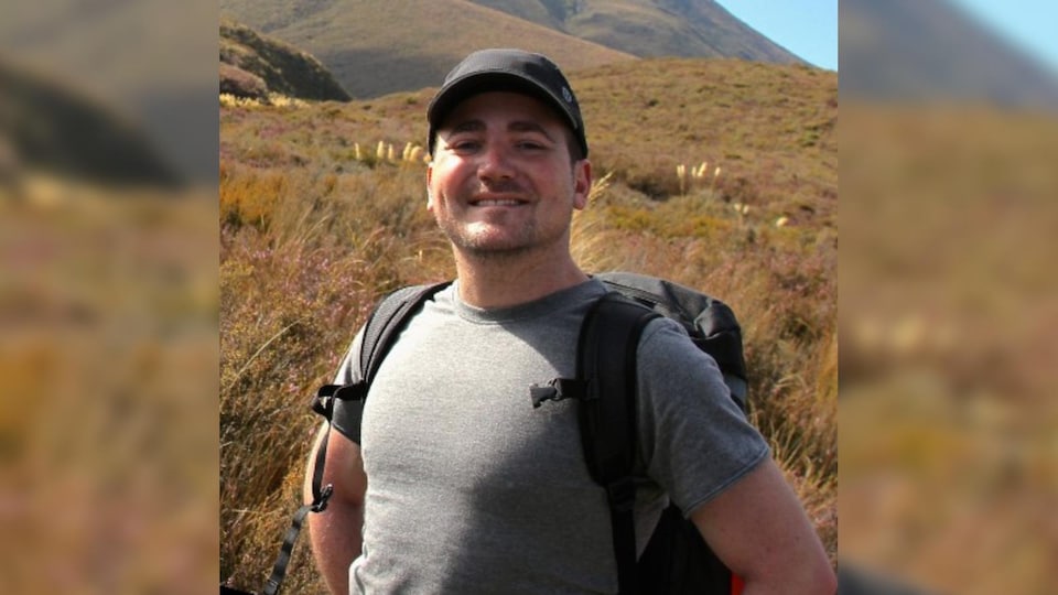 Brian Nadler, lors d'une marche en montagne, avec un sac à dos, sourit à la caméra.