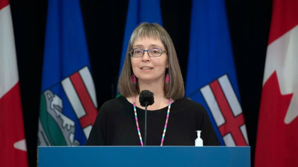 La médecin hygiéniste en chef de l'Alberta à un podium. Elle porte des lunettes et une frange.