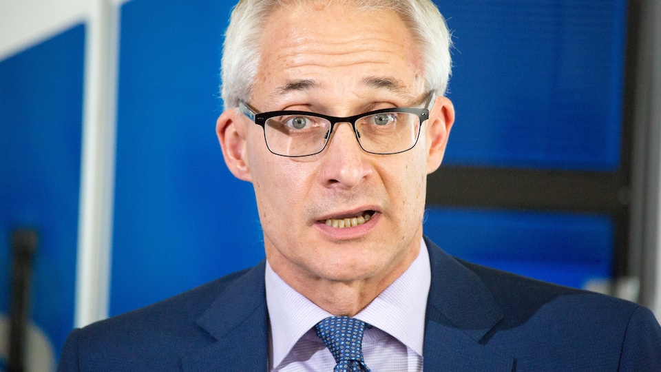Un homme dans un complet bleu parle en conférence de presse.