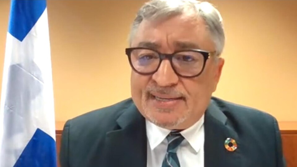 Le Dr Arruda est assis à un bureau avec un drapeau du Québec derrière lui.