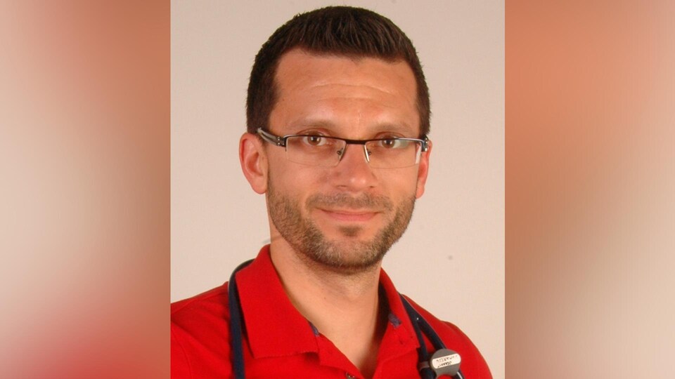 Portrait du médecin portant des lunettes et un polo rouge.