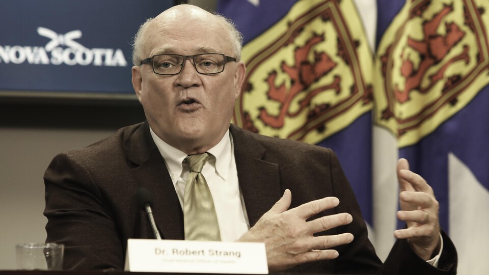 Robert Strang explique quelque chose en conférence de presse.