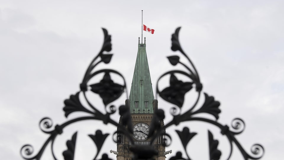 Le drapeau canadien en berne sur le parlement, vu à travers la grille d'entrée.