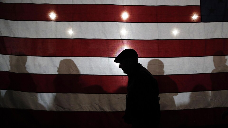Un homme dans l'ombre marche devant un drapeau américain géant.