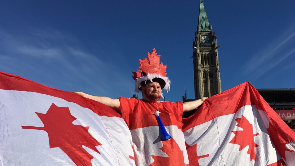 Un homme vêtu du plusieurs drapeaux canadiens formant une cape, avec un chapeau en feuille d'érable, sur la colline du parlement à Ottawa, le 1er juillet 2019.