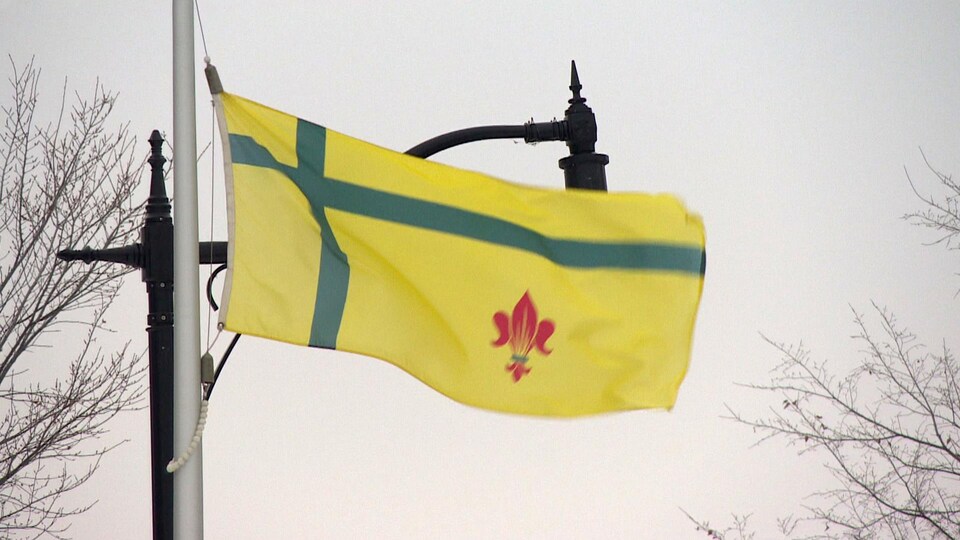 Un drapeau au haut d'un mat qui flotte dans le vent. Le drapeau est jaune avec un fleur de lys rouge.