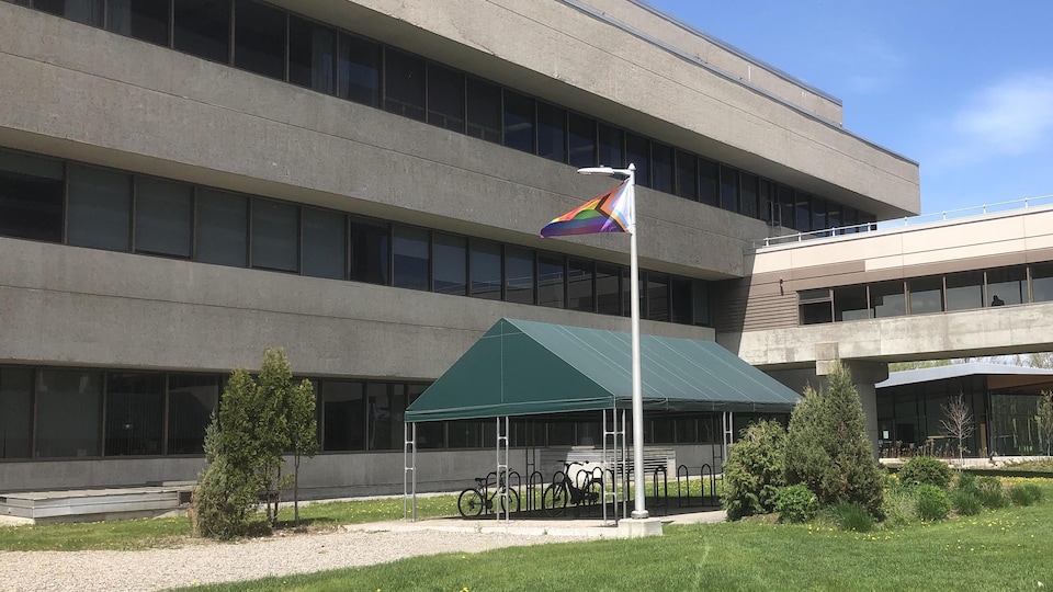 Un drapeau arc-en-ciel flotte devant un édifice.