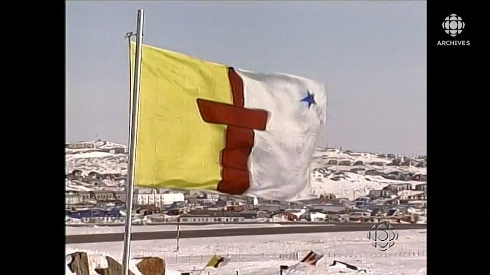 Le drapeau du Nunavut orné en son centre d'un inuksuk flottant au vent.