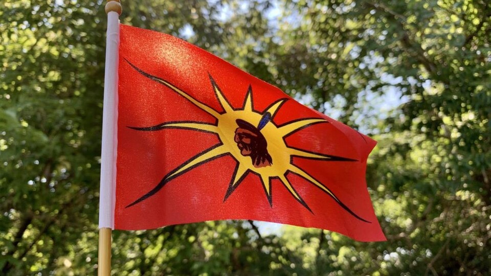 Le drapeau, sur lequel se trouve la tête d'un guerrier mohawk, flotte devant des arbres.