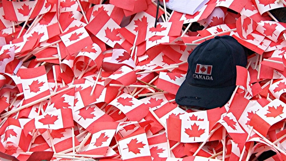 Une casquette avec un drapeau canadien déposée sur un amas de drapeaux du Canada.