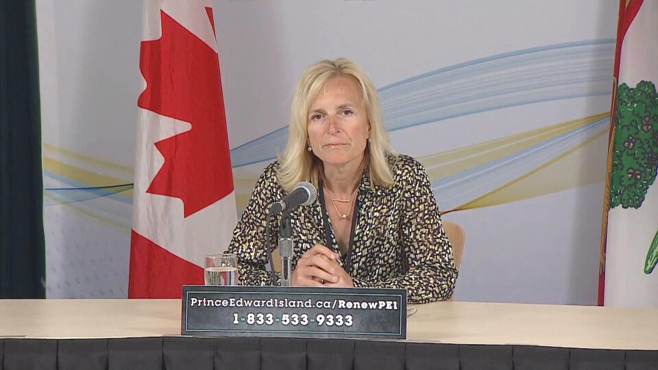 Heather Morrison assise à une table devant un drapeau du Canada et un drapeau de l'Île-du-Prince-Édouard.