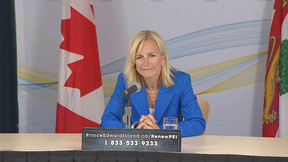 Heather Morrison assise à une table devant un drapeau du Canada et un drapeau de l'Île-du-Prince-Édouard.