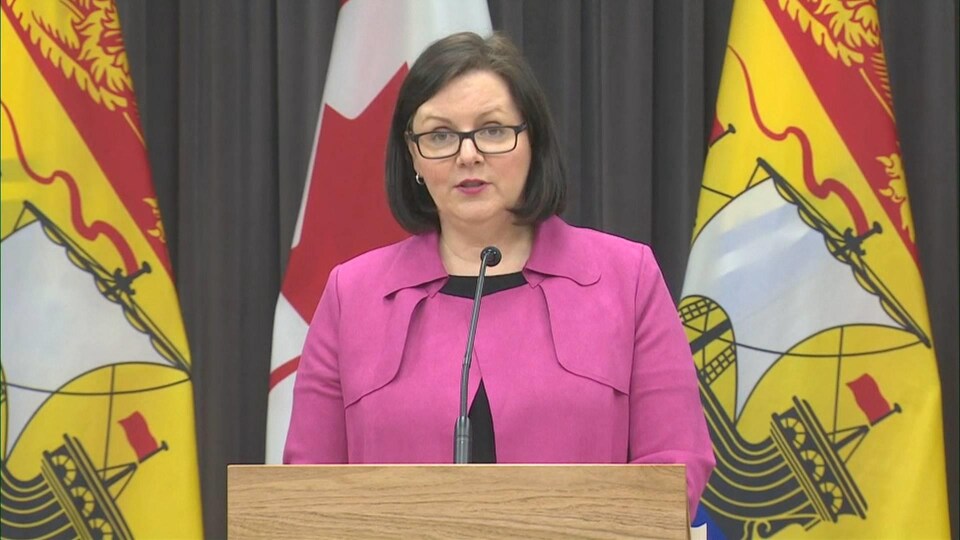 Jennifer Russell au lutrin devant des drapeaux.