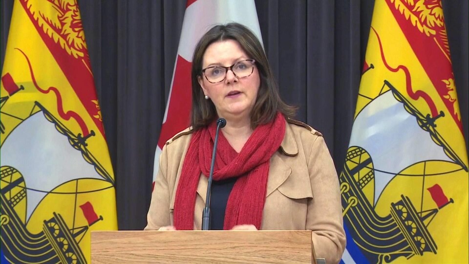 Jennifer Russell en conférence de presse devant des drapeaux du Nouveau-Brunswick.