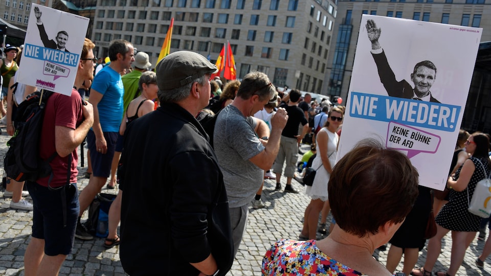 Des manifestants tiennent des pancartes sur lesquelles un homme fait le salut nazi. 