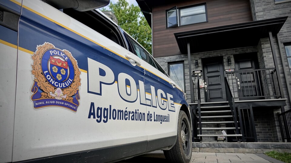 Une voiture de police du Service de police de l'agglomération de Longueuil est stationnée devant une résidence perquisitionnée.