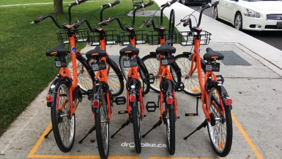 Cinq vélos de Dropbike prêts garés dans une zone délimitée par une ligne jaune sont prêts à être loués.