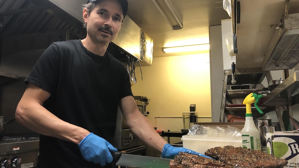 Un homme en cuisine découpe de la viande avec un couteau.