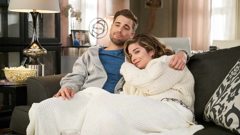 L'acteur Dustin Milligan et l'actrice Annie Murphy de la série Bienvenue à Schitt's Creek sont assis sur un canapé.