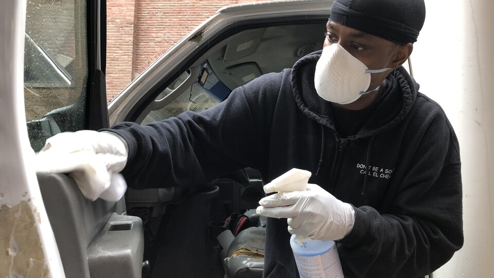 Dwayne Ramgeet en train de laver le camion, il est noir et porte un petit bonnet noir, il a un sweet noir, il a des gants et un masque de médecine pour se protéger