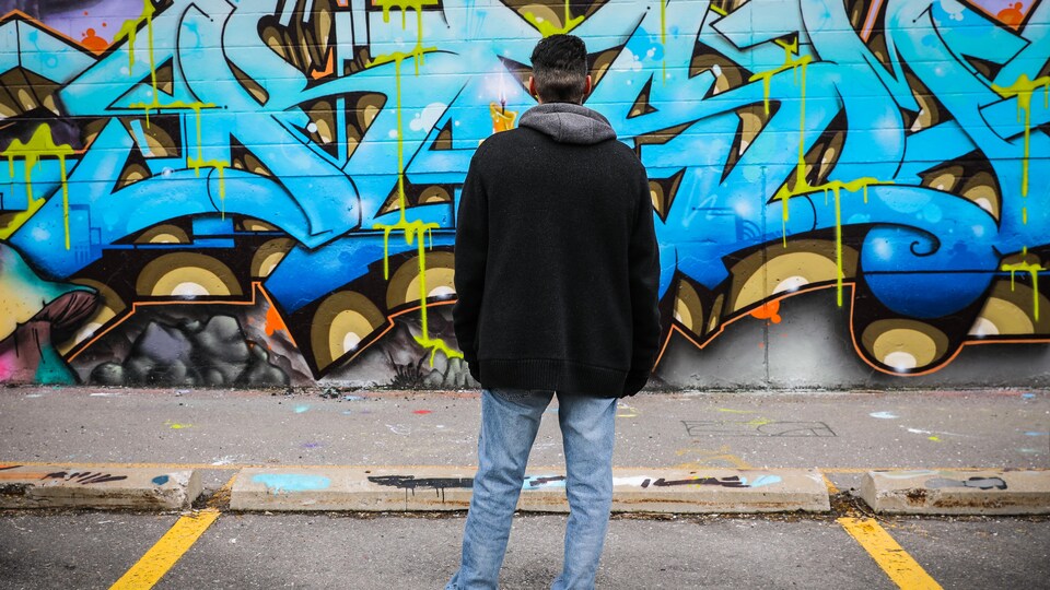 Un homme de dos face à un mur de graffitis.