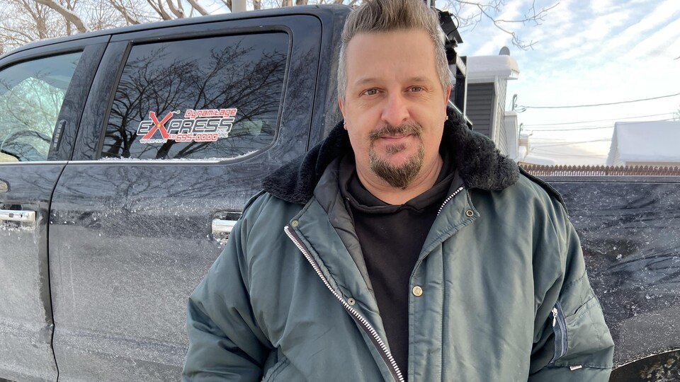 Un homme se tient debout devant une camionnette l'hiver.