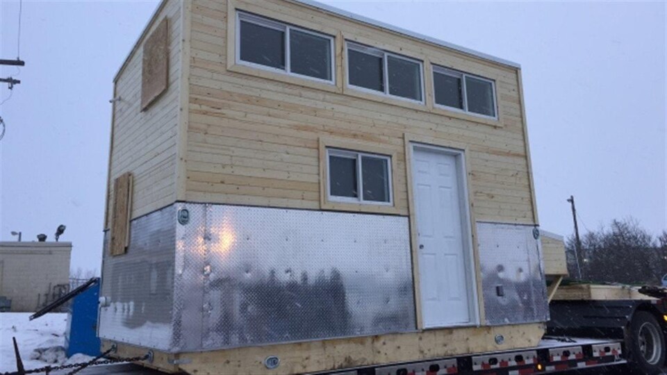 Une petite maison en bois et en métal sur la remorque d'un camion.